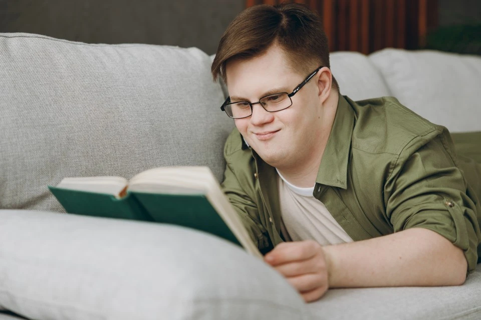 Disabled man with down syndrome relaxing on couch at home with a book
