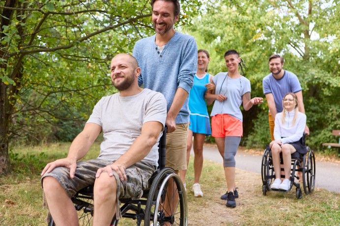 Disabled man and woman in wheelchairs out for a walk with group of friends